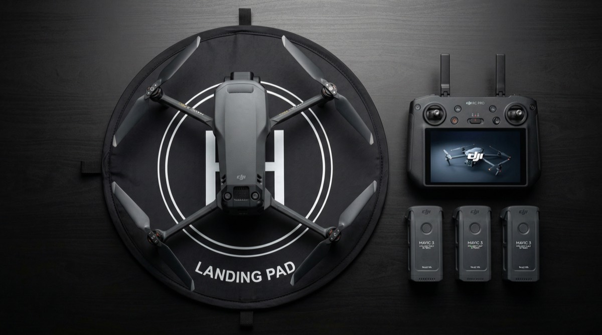Professional DJI Mavic drone on black landing pad next to controller and spare batteries