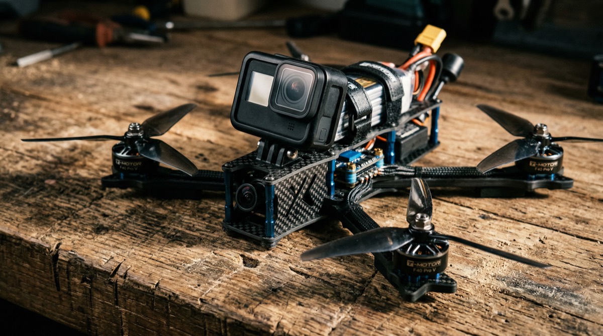 FPV drone with exposed carbon fibre frame and four propellers on wooden surface with dramatic side lighting